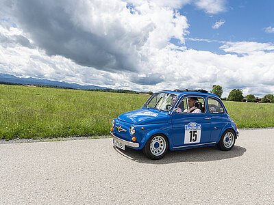 Blauer Fiat 500 mit Startnummer 15 auf einer Landstraße an einem sonnigen Tag.